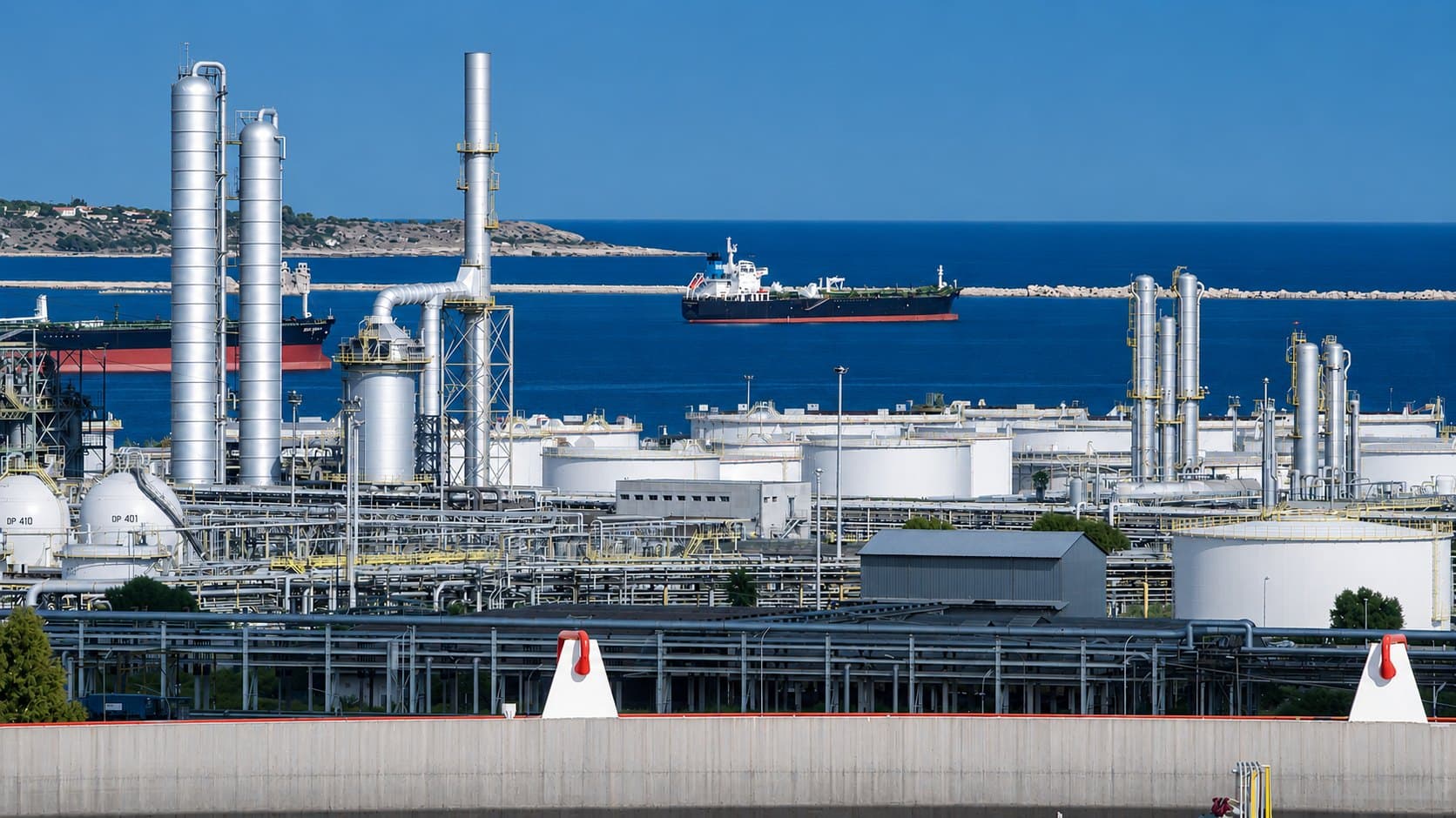 Gli impianti visti dalla costa, con una petroliera alla fonda e le colonne di raffinazione in primo piano.